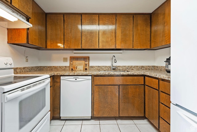 kitchen with white appliances, brown cabinetry, light tile patterned flooring, a sink, and under cabinet range hood