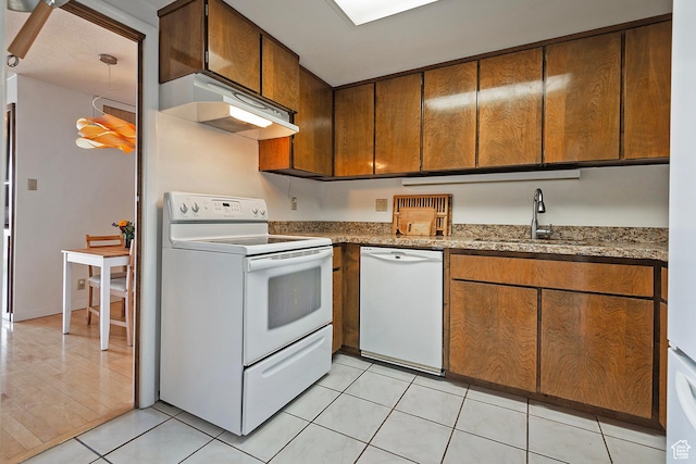 kitchen featuring white appliances, light stone counters, light tile patterned floors, a sink, and under cabinet range hood