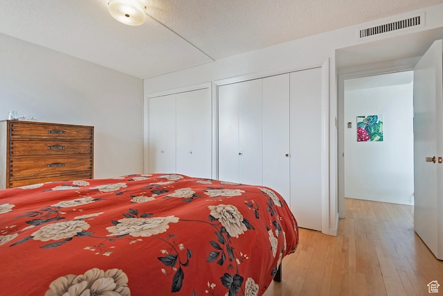 bedroom featuring visible vents, a textured ceiling, light wood-style floors, and multiple closets