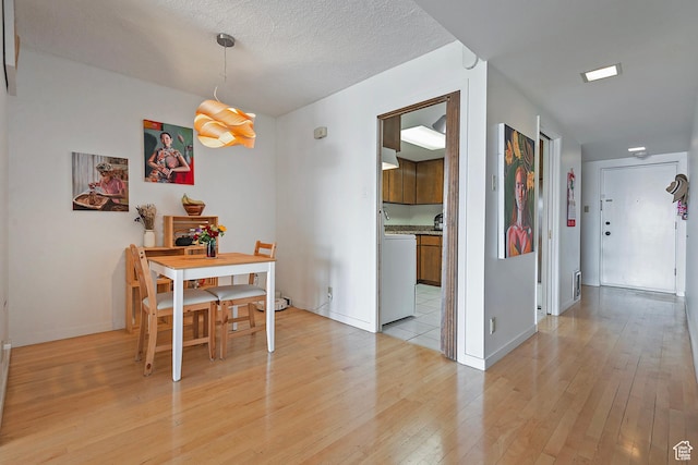 dining space with light wood finished floors, visible vents, a textured ceiling, and baseboards