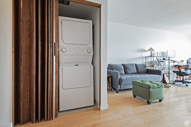 clothes washing area featuring laundry area, light wood-style flooring, stacked washer and clothes dryer, and a textured ceiling