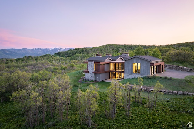 9774 N Red Hawk Trl, Park City, UT 84098 - back of property at dusk featuring a wooded view, concrete driveway, a chimney, and a garage