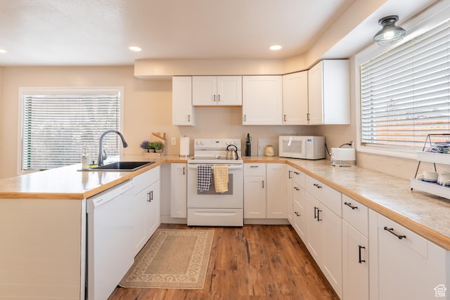 kitchen with white appliances, a peninsula, a sink, light countertops, and white cabinets