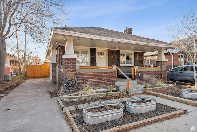 view of front of house with a porch, brick siding, fence, and a chimney