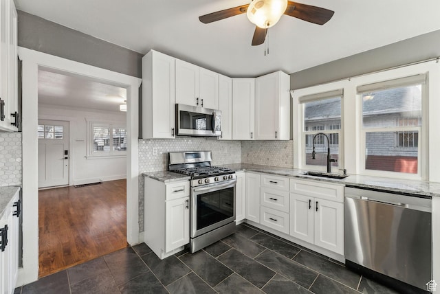 kitchen featuring a sink, appliances with stainless steel finishes, a ceiling fan, and light stone counters