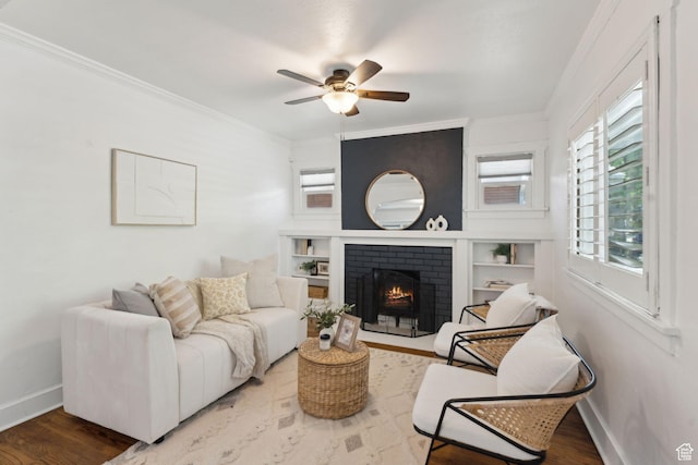 living room featuring baseboards, ornamental molding, ceiling fan, and a fireplace