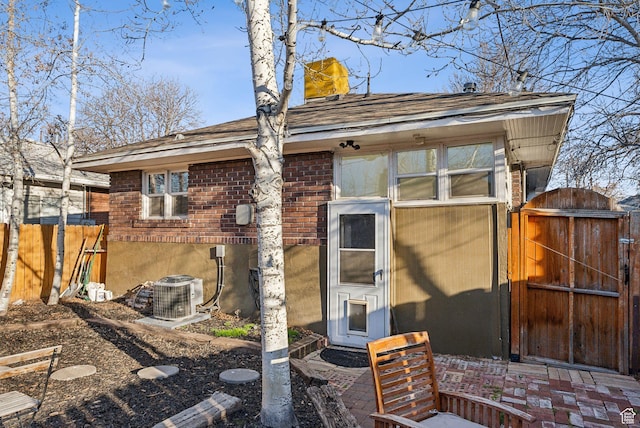 rear view of house featuring a chimney, a gate, brick siding, fence, and cooling unit