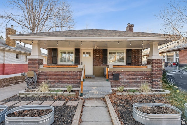 view of front facade with brick siding, covered porch, and a chimney