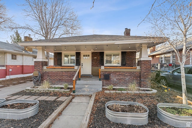 view of front of property featuring covered porch, brick siding, and a chimney
