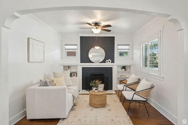 living area featuring a ceiling fan, crown molding, a fireplace, wood finished floors, and baseboards