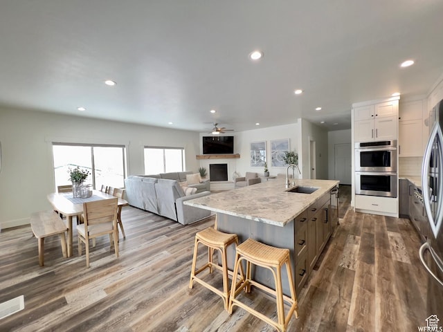833 W Sunrise Cir, Garden City, UT 84028 - kitchen with an island with sink, light stone counters, a sink, a fireplace, and appliances with stainless steel finishes