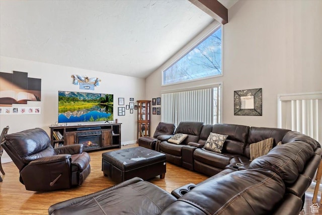 living area with wood finished floors, baseboards, high vaulted ceiling, a glass covered fireplace, and beamed ceiling
