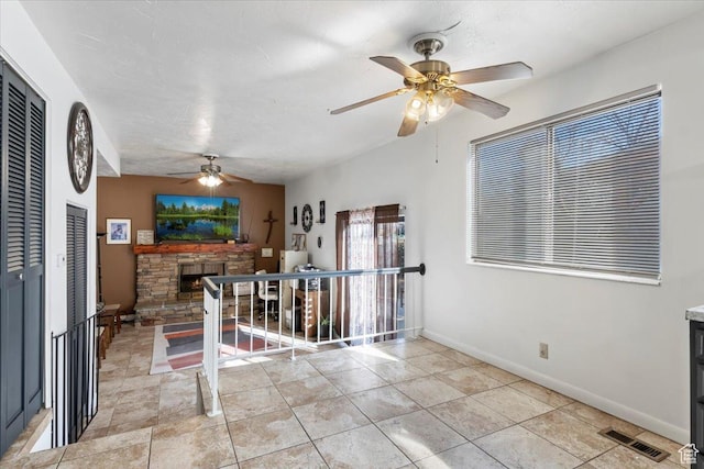 interior space with visible vents, a ceiling fan, a stone fireplace, light tile patterned floors, and baseboards