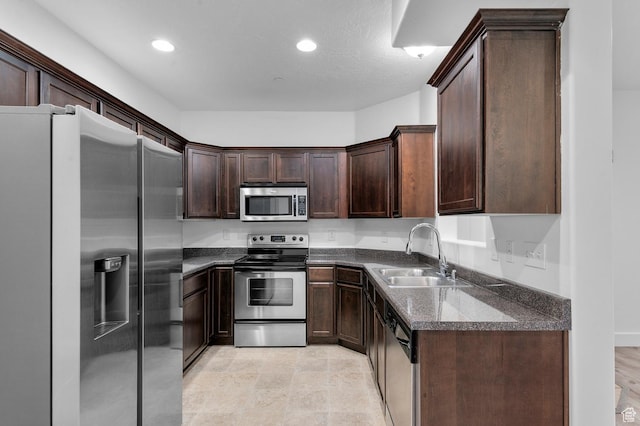 kitchen with dark stone countertops, recessed lighting, a sink, stainless steel appliances, and dark brown cabinets