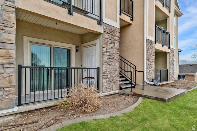 entrance to property with stucco siding, stone siding, and a balcony