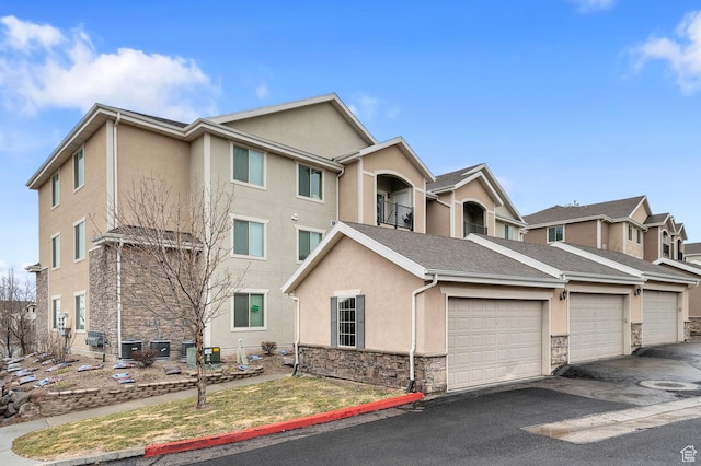 view of front facade with central AC unit, driveway, stucco siding, and stone siding