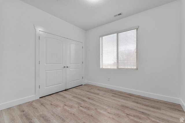 unfurnished bedroom with a closet, visible vents, baseboards, and wood finished floors