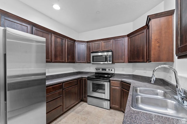 kitchen with a sink, appliances with stainless steel finishes, dark countertops, dark brown cabinetry, and recessed lighting