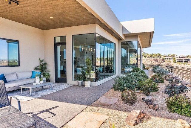 view of exterior entry featuring stucco siding, an outdoor hangout area, fence, and a patio area