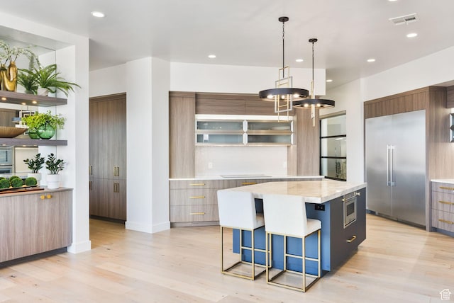 kitchen with visible vents, modern cabinets, stainless steel built in refrigerator, a breakfast bar, and a kitchen island