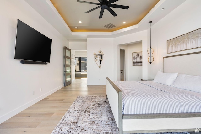 bedroom with visible vents, a raised ceiling, baseboards, and light wood finished floors