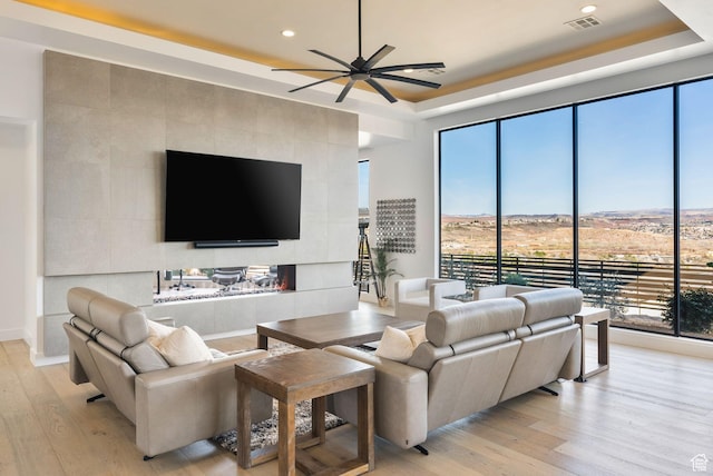 living room featuring a raised ceiling, light wood-style floors, and ceiling fan