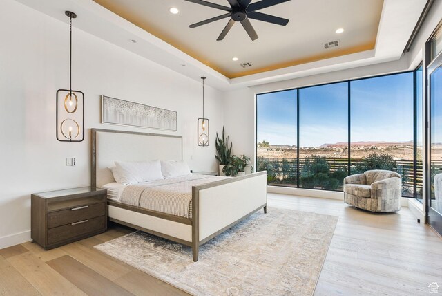 bedroom with a raised ceiling, visible vents, and light wood-type flooring