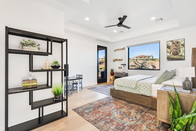 bedroom featuring wood finished floors, visible vents, a tray ceiling, recessed lighting, and access to exterior