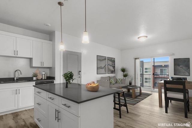 kitchen with a sink, light wood-style floors, dark countertops, and a center island
