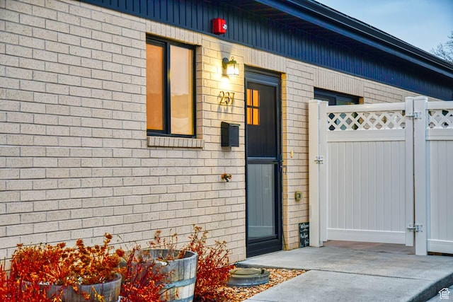 doorway to property with brick siding, fence, and a gate