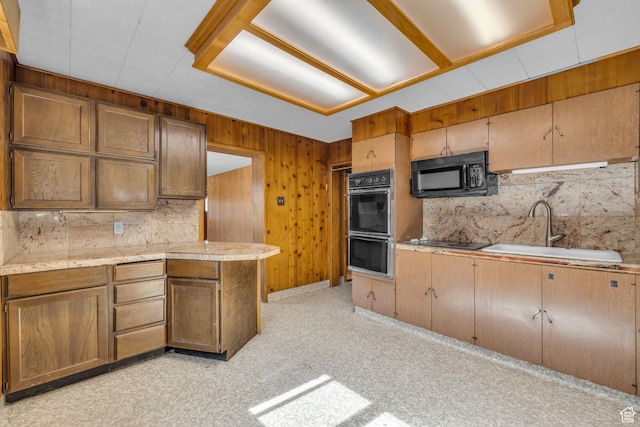 kitchen featuring a sink, black appliances, light countertops, wood walls, and light carpet