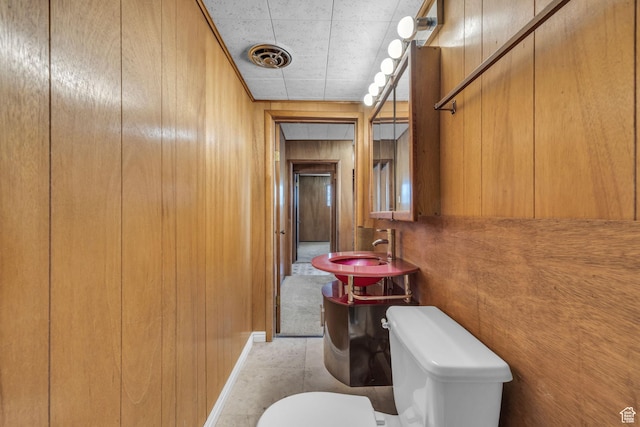 bathroom featuring a sink, toilet, and wooden walls