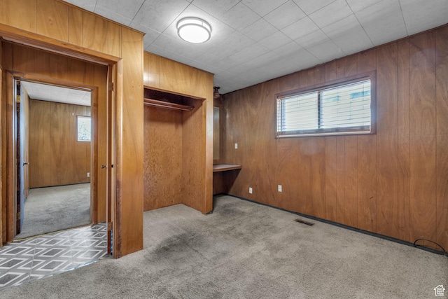 unfurnished bedroom featuring visible vents, carpet floors, wooden walls, and a closet