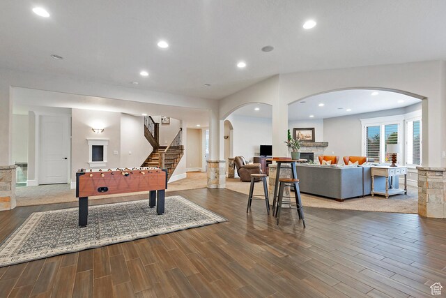 recreation room featuring wood finished floors, arched walkways, a fireplace, recessed lighting, and baseboards