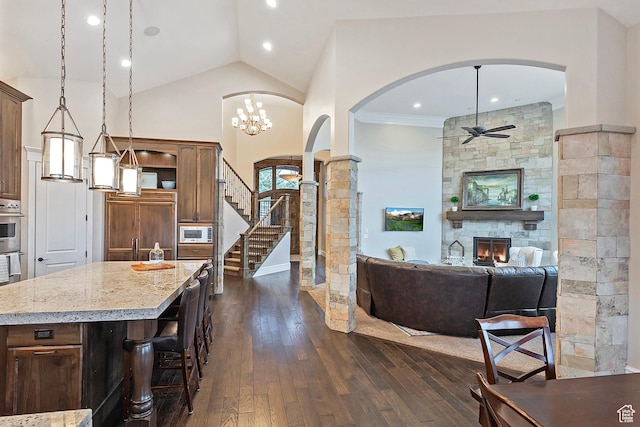 living area with arched walkways, ceiling fan, dark wood-style floors, a stone fireplace, and decorative columns
