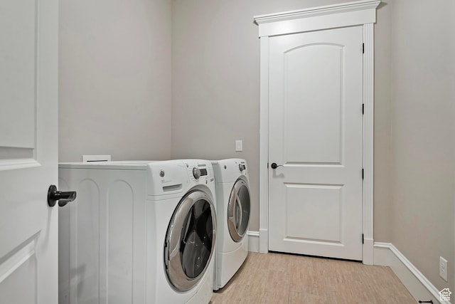 laundry room with washing machine and dryer, baseboards, and light wood-type flooring