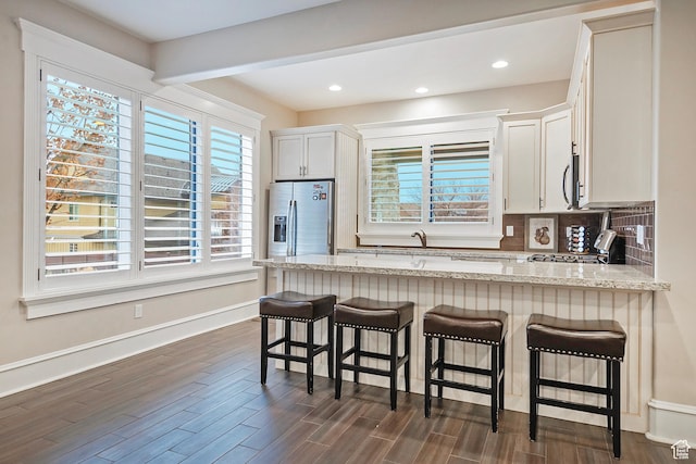 kitchen with stainless steel appliances, light stone counters, a peninsula, backsplash, and a breakfast bar area