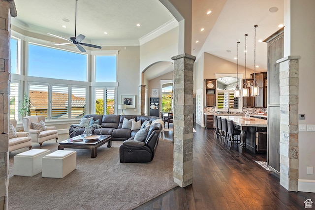 living room featuring ornate columns, ceiling fan, arched walkways, dark wood-type flooring, and ornamental molding