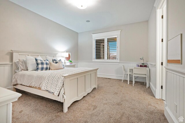 bedroom featuring a wainscoted wall and light carpet