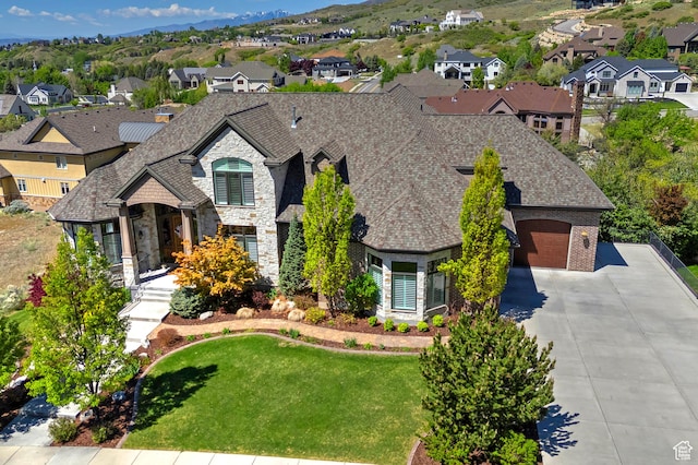 french provincial home featuring stone siding, concrete driveway, a residential view, an attached garage, and a front lawn