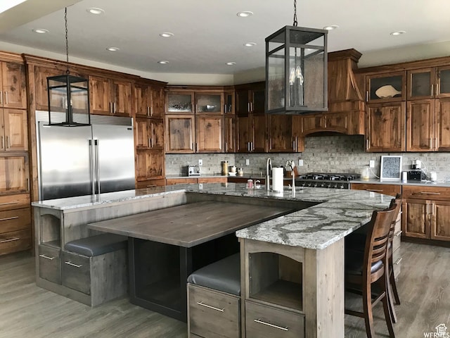 kitchen with tasteful backsplash, glass insert cabinets, light wood-type flooring, and built in fridge
