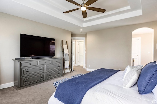 bedroom with a ceiling fan, arched walkways, a tray ceiling, light colored carpet, and baseboards