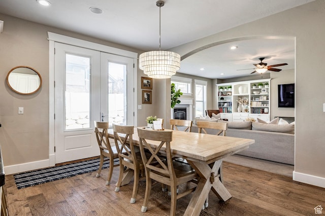 dining area with wood finished floors, arched walkways, baseboards, a glass covered fireplace, and ceiling fan