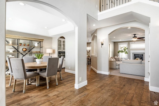 dining area with wood finished floors, a glass covered fireplace, ceiling fan, arched walkways, and baseboards