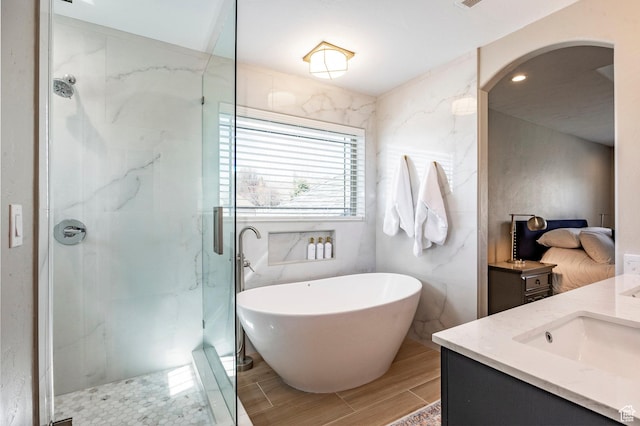 bathroom with a freestanding bath, vanity, a marble finish shower, tile walls, and wood finish floors