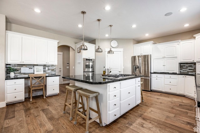 kitchen with dark countertops, decorative backsplash, arched walkways, stainless steel appliances, and dark wood-style flooring