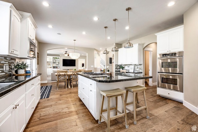 kitchen with arched walkways, light wood finished floors, backsplash, appliances with stainless steel finishes, and a kitchen island