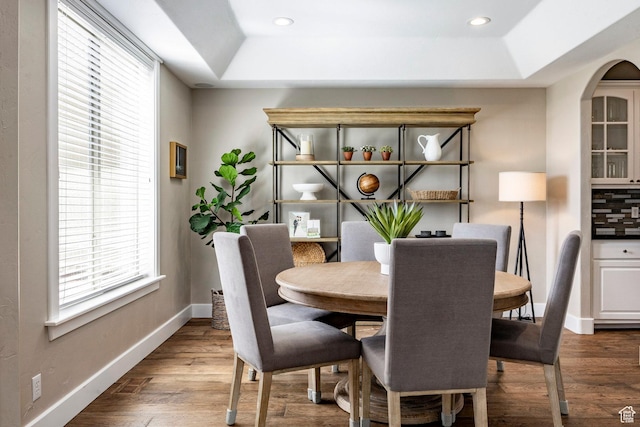 dining space with dark wood-type flooring, a raised ceiling, baseboards, and recessed lighting