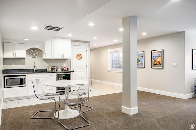 kitchen with wine cooler, stainless steel microwave, dark countertops, visible vents, and white cabinetry