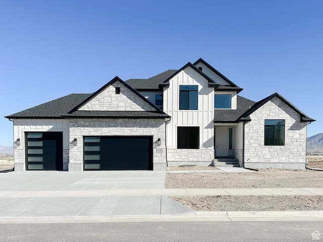 view of front of property with an attached garage, stone siding, board and batten siding, and roof with shingles